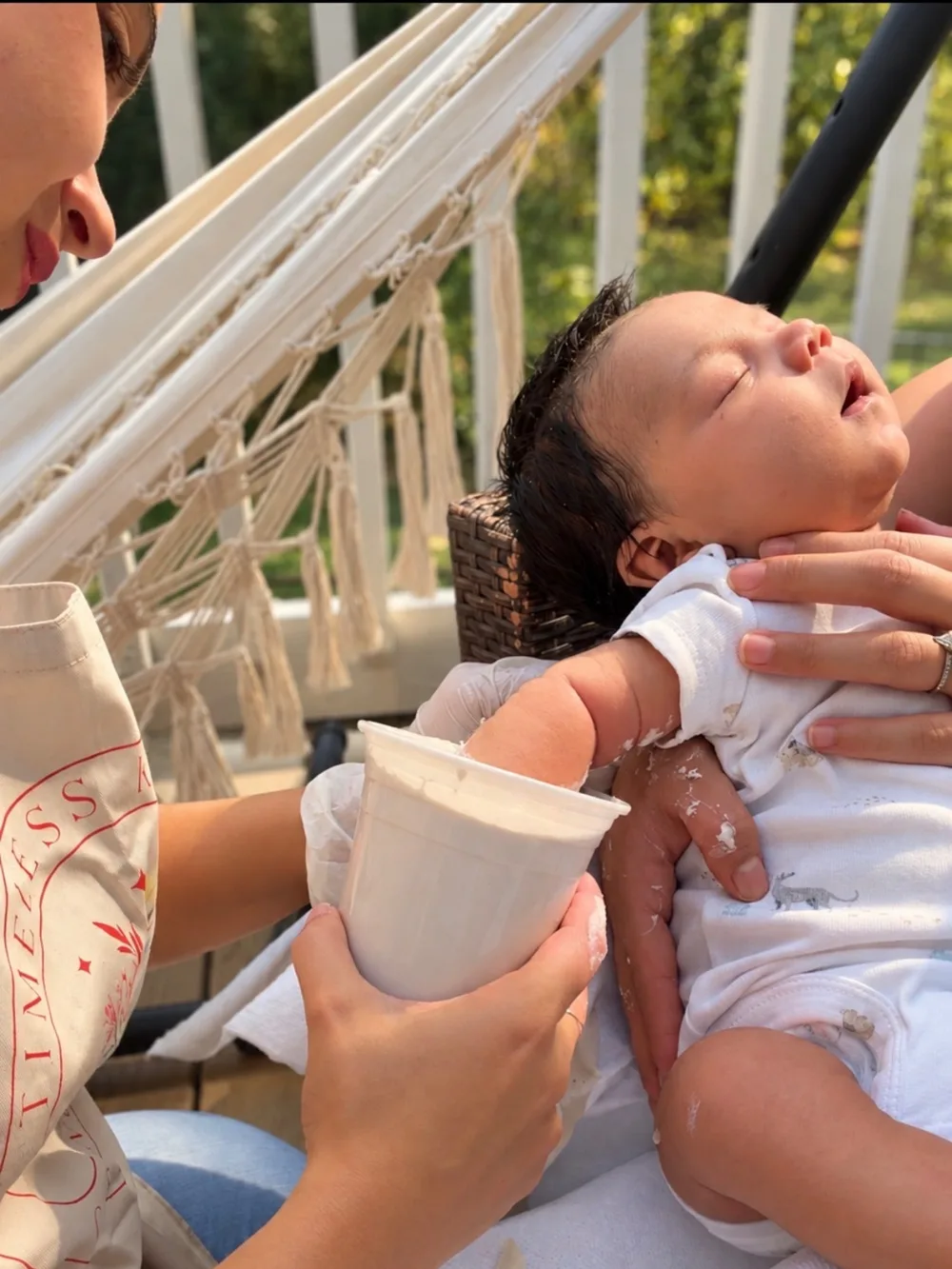 Maray holding a cup of alginate around a sleeping newborn's hand while a parent cradles the baby